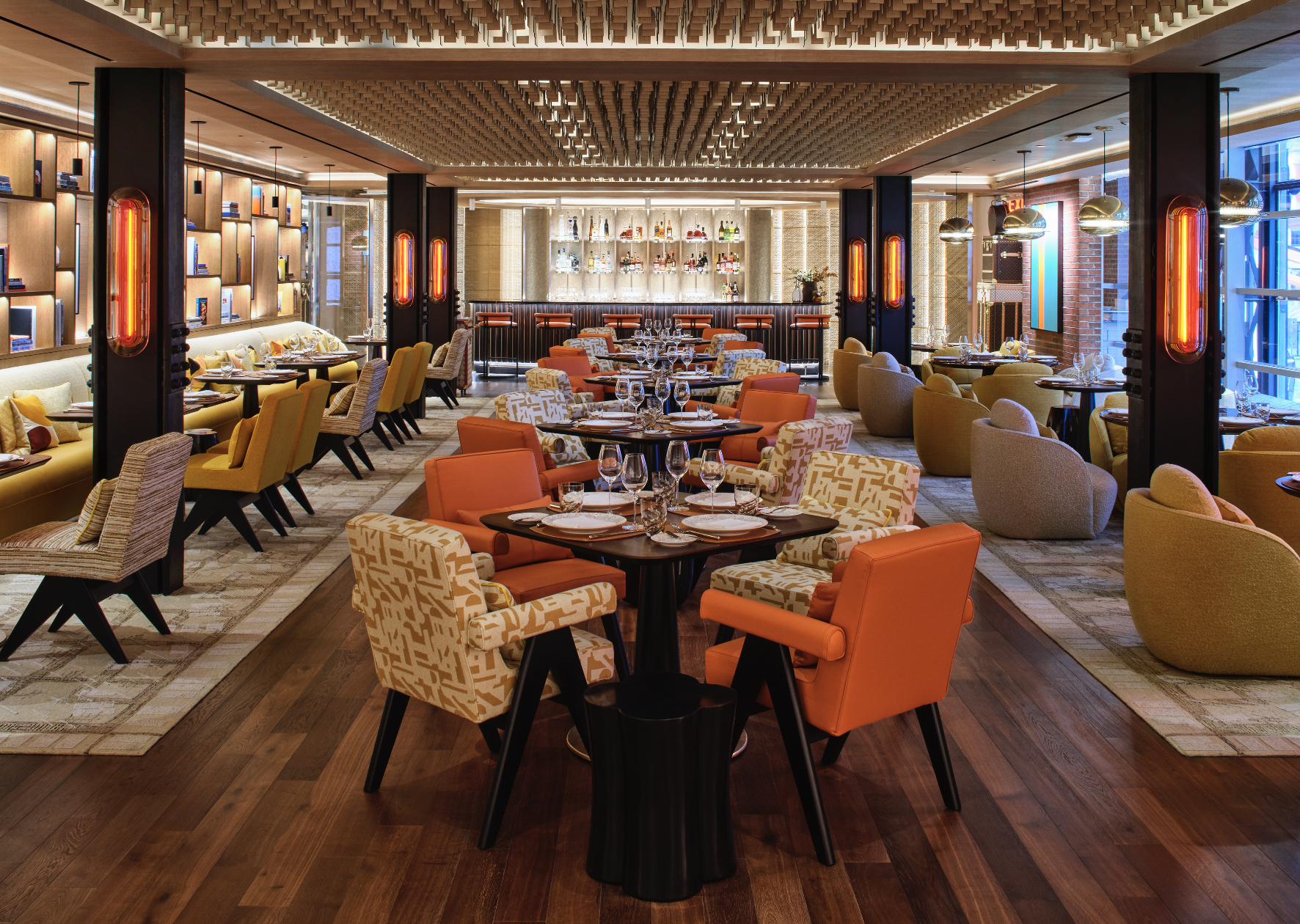 Interior de Le Café Louis Vuitton en la calle 57 de Nueva York, con sillones naranjas, mesas preparadas y estanterías de libros iluminadas