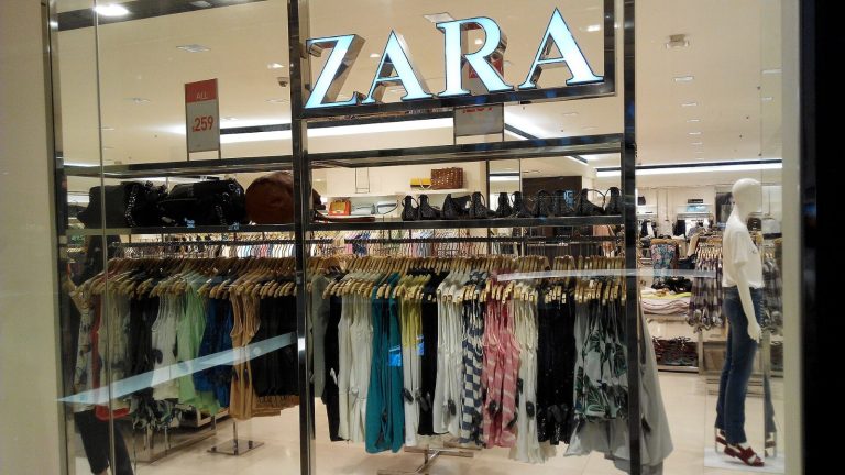 Interior de una tienda de Zara con el logotipo de la marca y percheros llenos de ropa