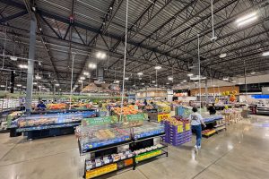 Interior de una tienda Kroger Marketplace con expositores de producto y una clienta caminando por el pasillo central