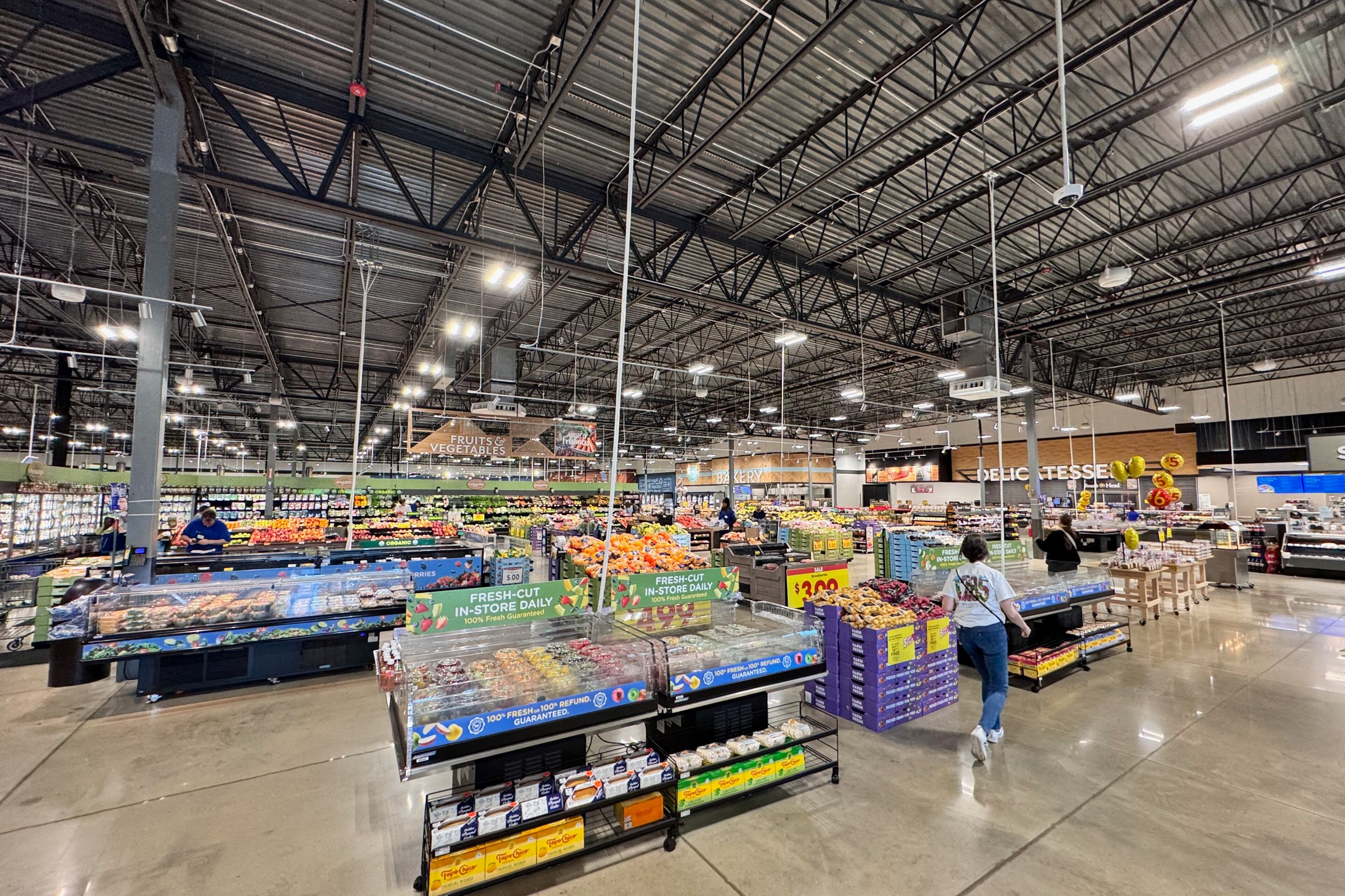 Interior de una tienda Kroger Marketplace con expositores de producto y una clienta caminando por el pasillo central
