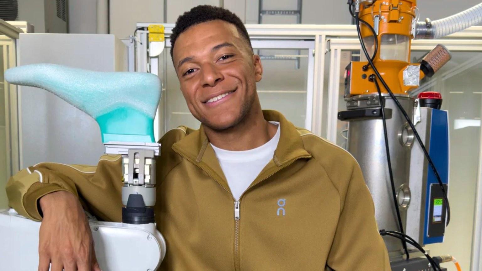 Kylian Mbappé apoyado en un brazo robótico junto a una plantilla de espuma en el laboratorio de innovación de On Running