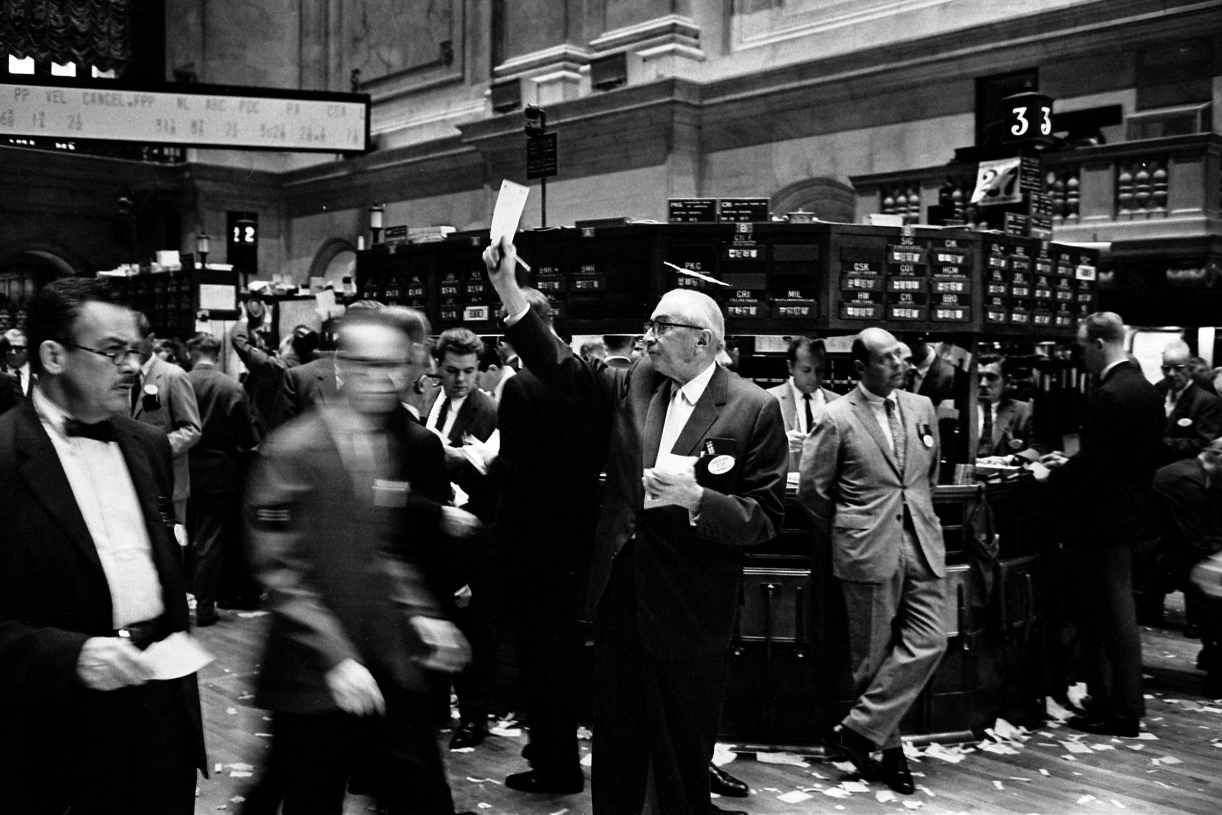 Operadores de bolsa trabajando en el parqué de la Bolsa de Nueva York, con papeles en el suelo y paneles de cotización al fondo
