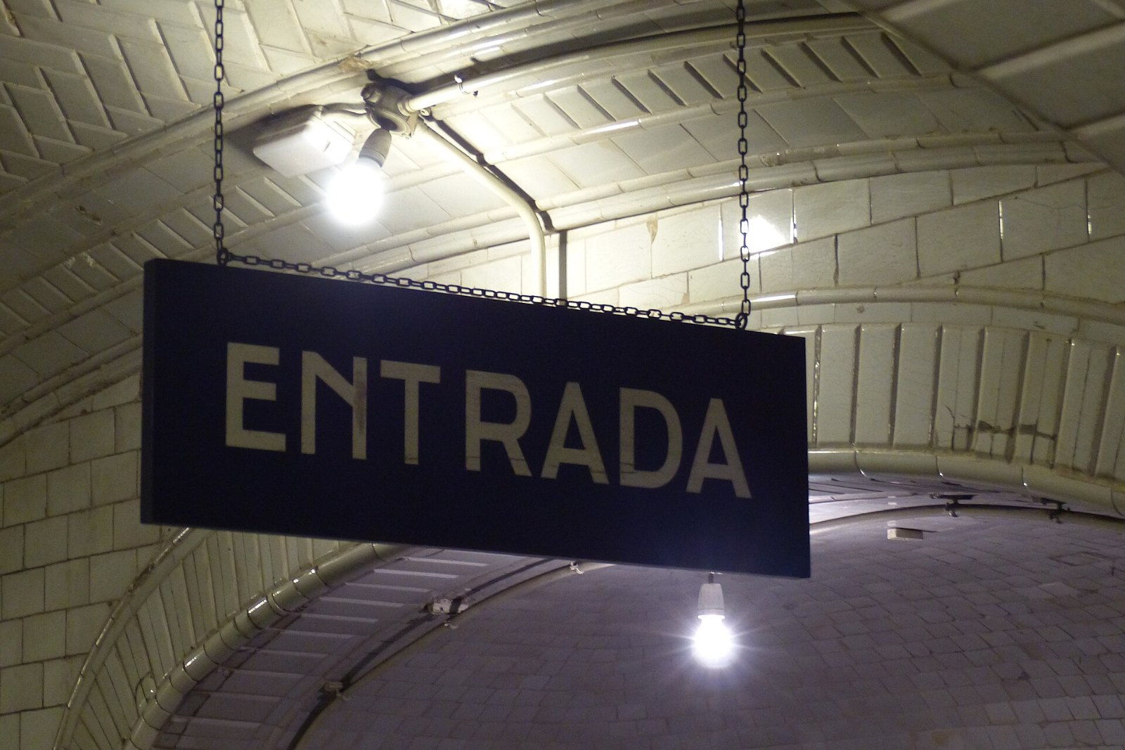 Cartel azul de «Entrada» colgado de la bóveda de azulejos blancos en la estación de Chamberí