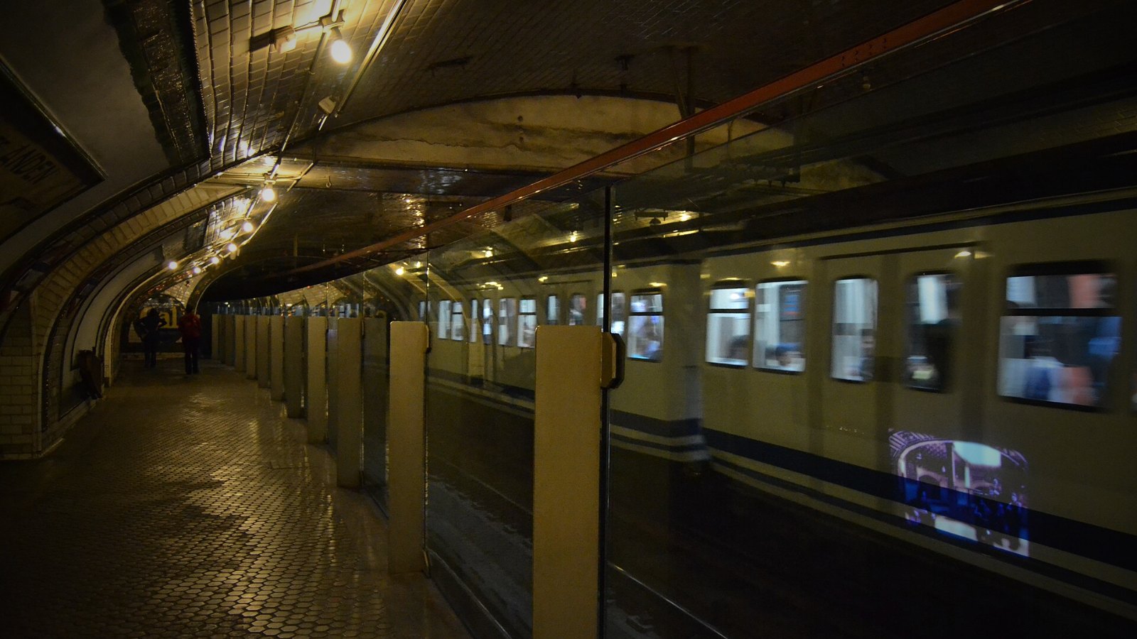 Andén de la estación fantasma de Chamberí del Metro de Madrid, con sus azulejos y bóveda, mientras un tren de la Línea 1 pasa sin detenerse