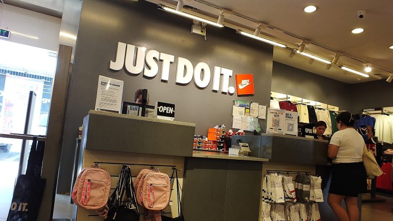 Mostrador de una Nike Factory Store (outlet) con el lema Just Do It en la pared, mochilas y calcetines en oferta