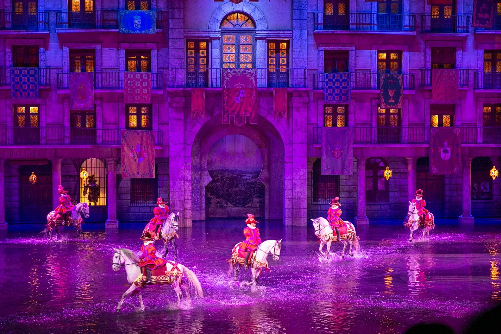Jinetes a caballo atraviesan una plaza inundada frente a un palacio iluminado en un espectáculo de Puy du Fou España en Toledo